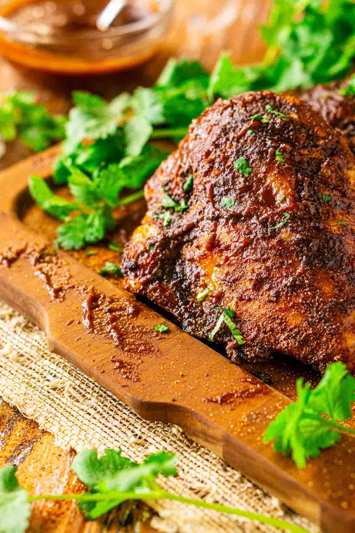 A close-up shot of the smoked chicken breast with a bowl of BBQ sauce in the background and cilantro on the side of the meat.