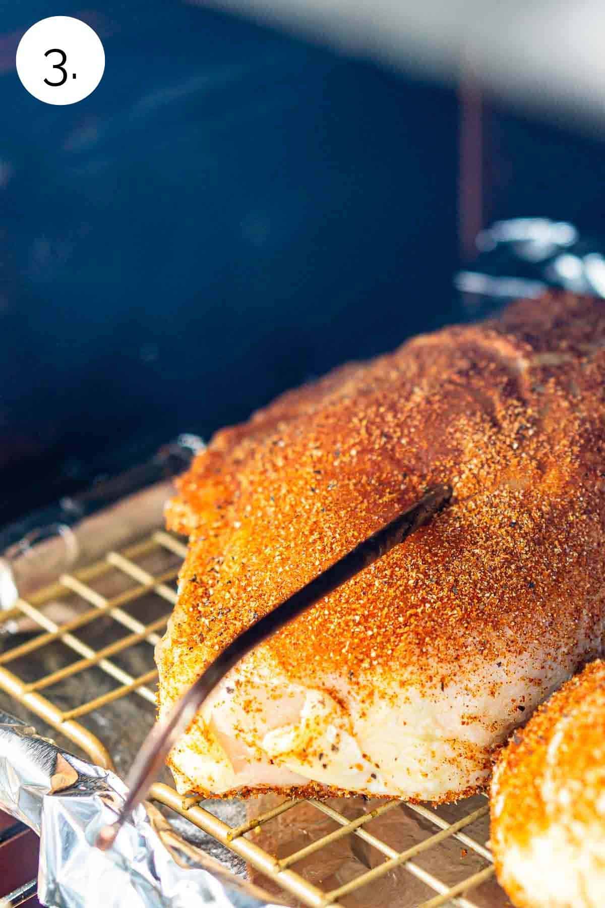 The chicken breasts in the smoker with a leave-in meat thermometer inserted in the thickest part of the meat.