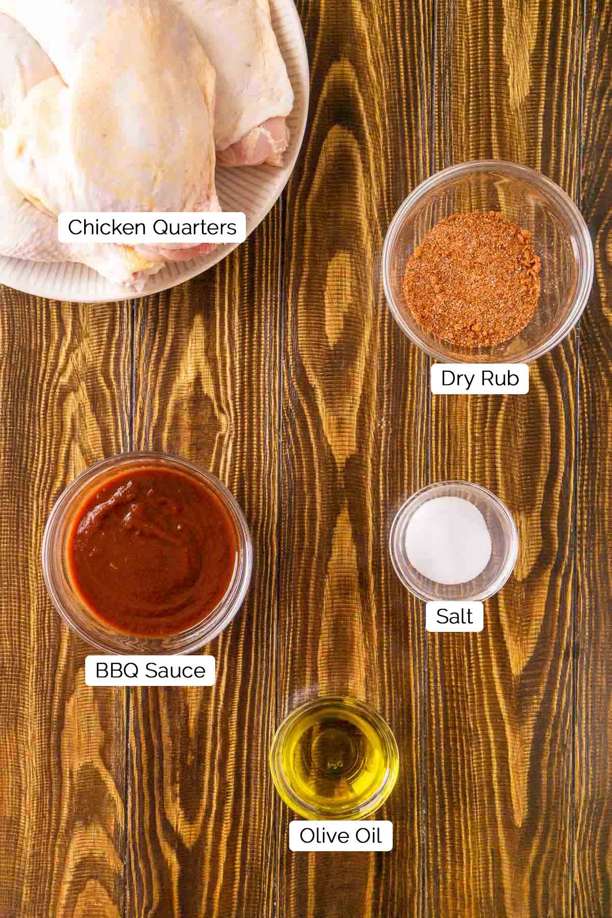 The ingredients for smoking the chicken on a brown wooden board with white and black labels underneath the items.