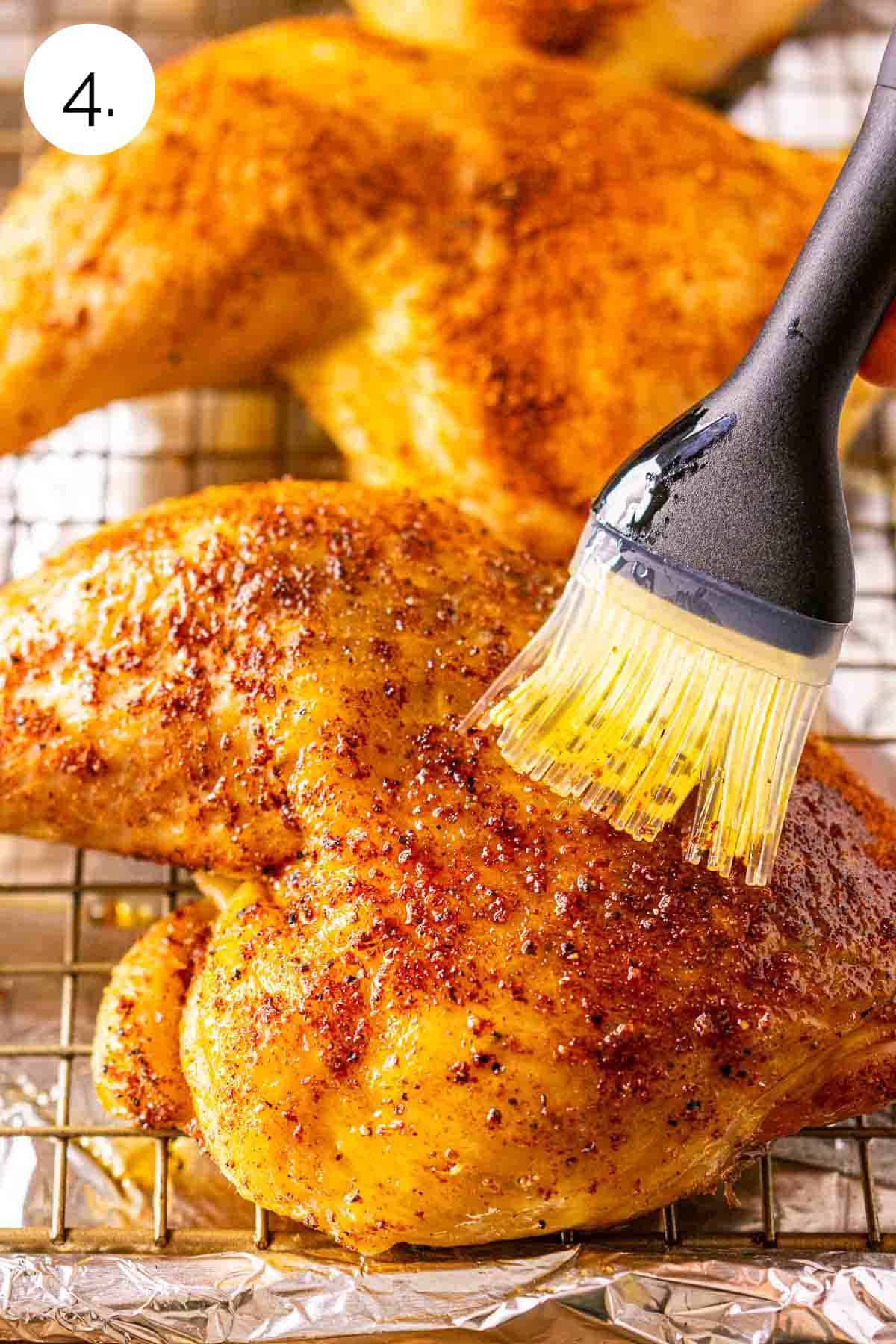 A silicone brush coating the chicken with olive oil on a wire rack over a baking sheet covered in aluminum foil.