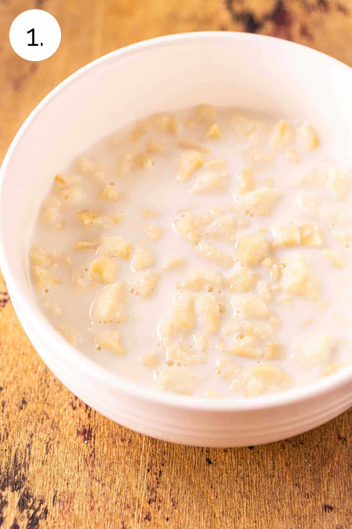 The soft bread crumbs soaking in a small white bowl full of milk on a wooden surface.