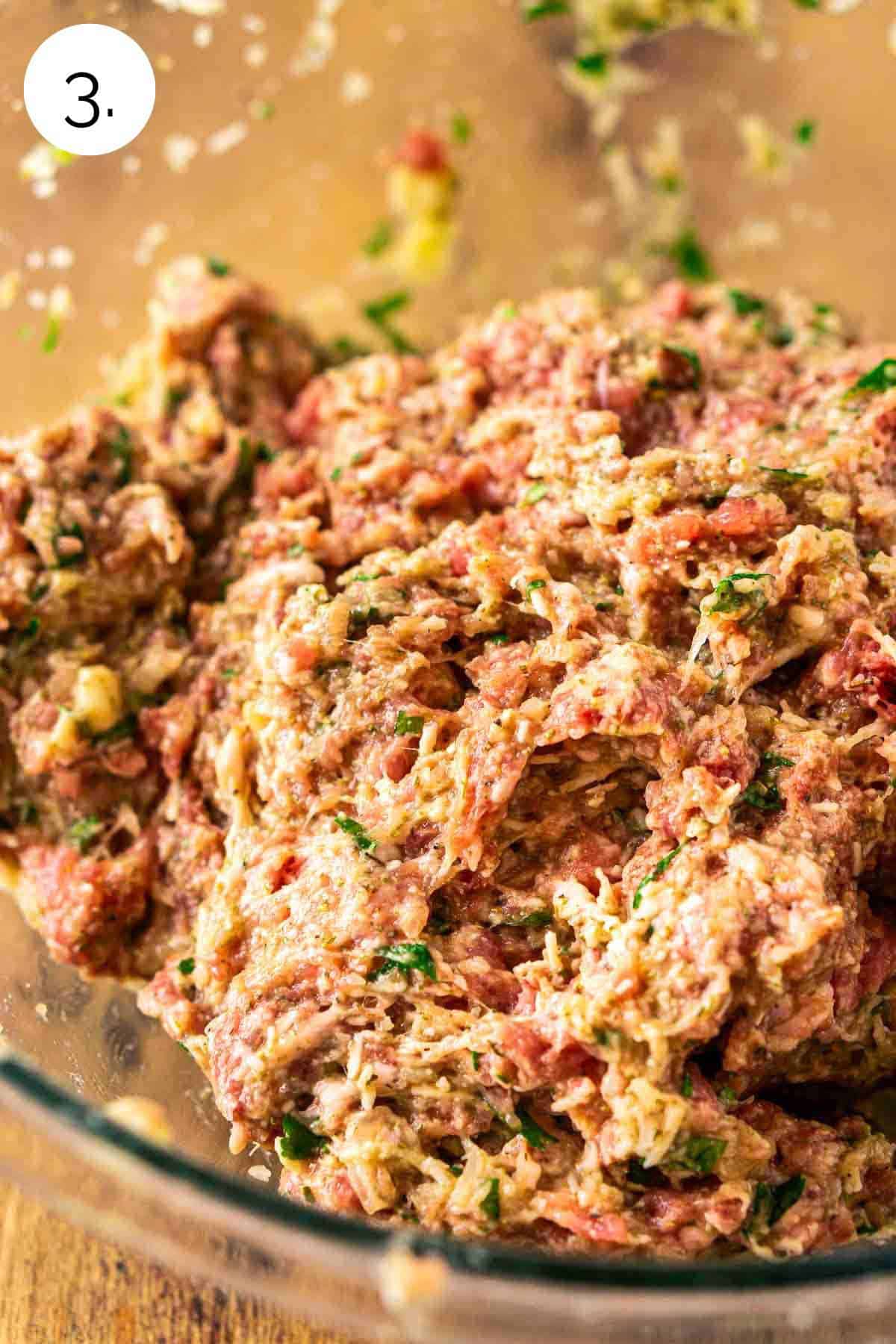 The ground beef and pork combined with the egg mixture in a large glass mixing bowl on a wooden surface.