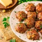 The smoked meatballs on a white plate set on top of burlap with a grated Parmesan and chopped parsley around it.