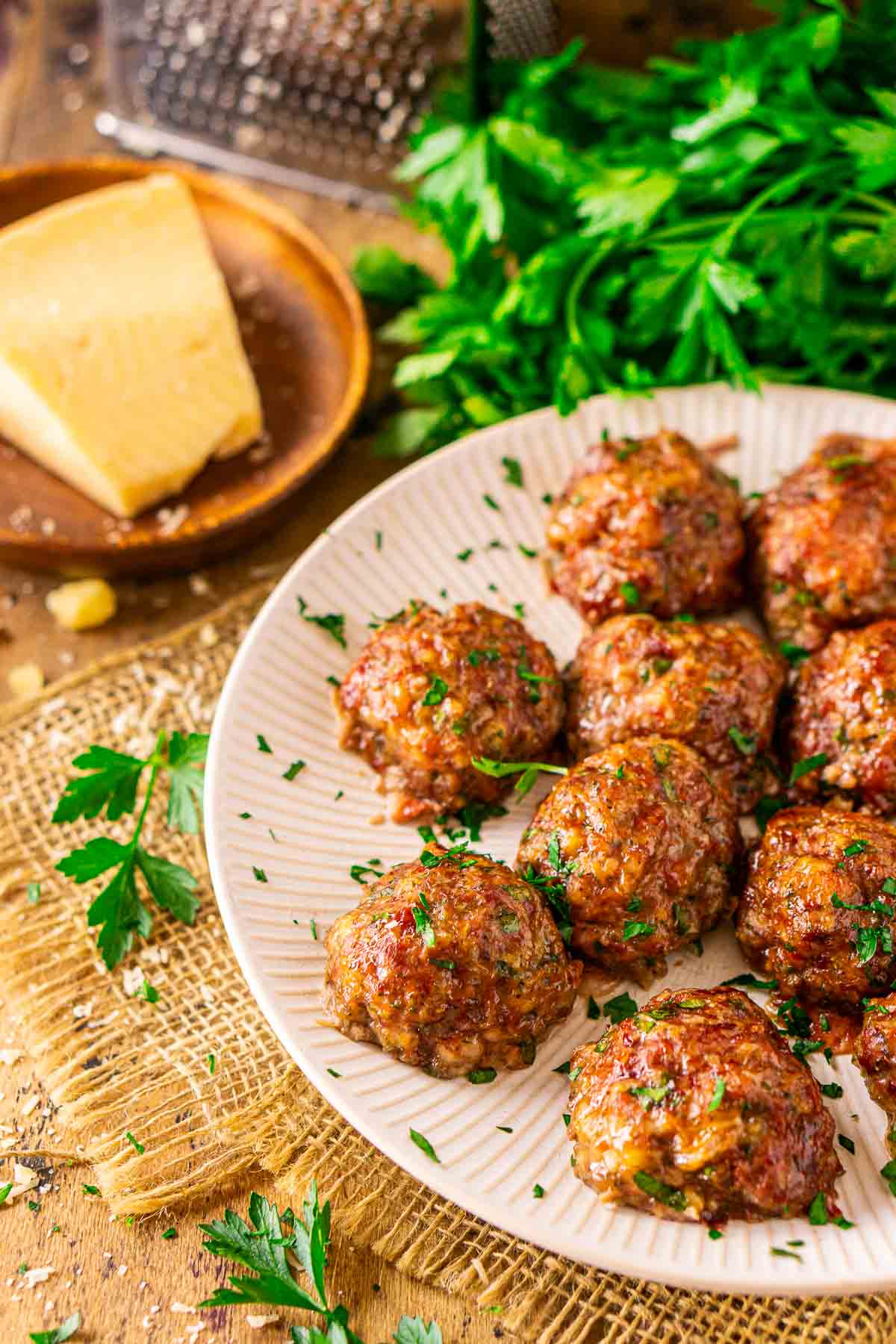 The smoked meatballs on a white plate set on top of burlap with a grated Parmesan and chopped parsley around it.