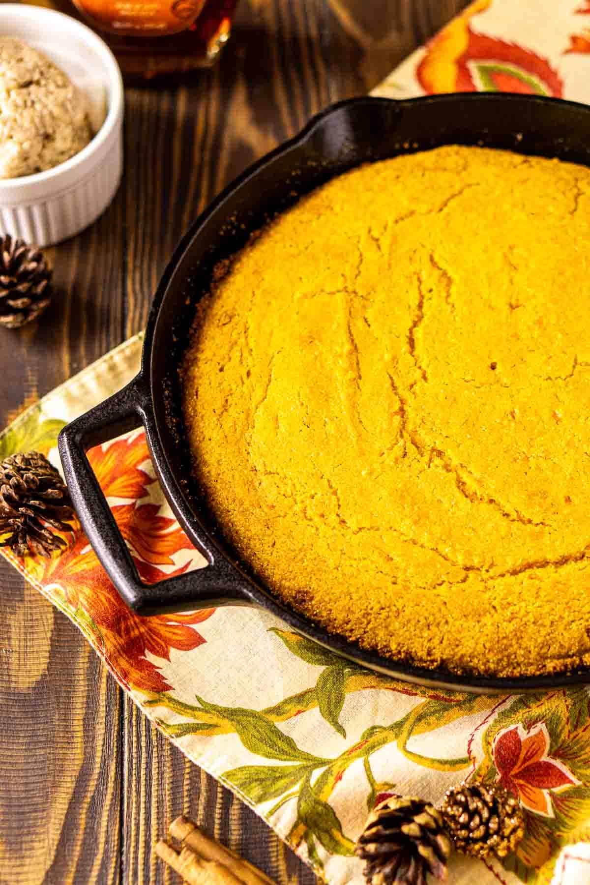 An aerial view of the sweet potato cornbread in a black cast-iron skillet with a ramekin of the maple butter on the left.