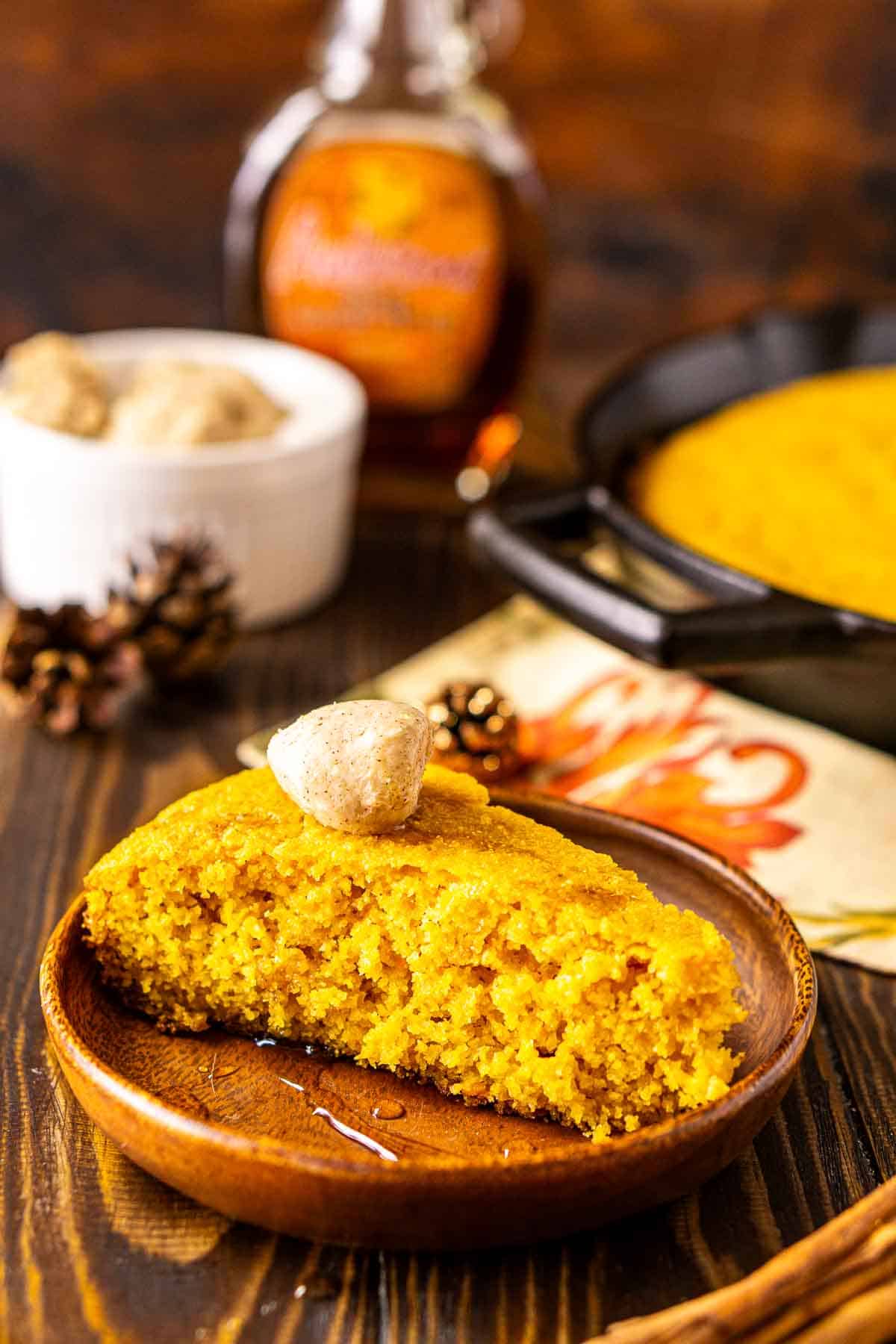 A slice of the sweet potato cornbread on a brown wooden plate with maple syrup drizzled around it.