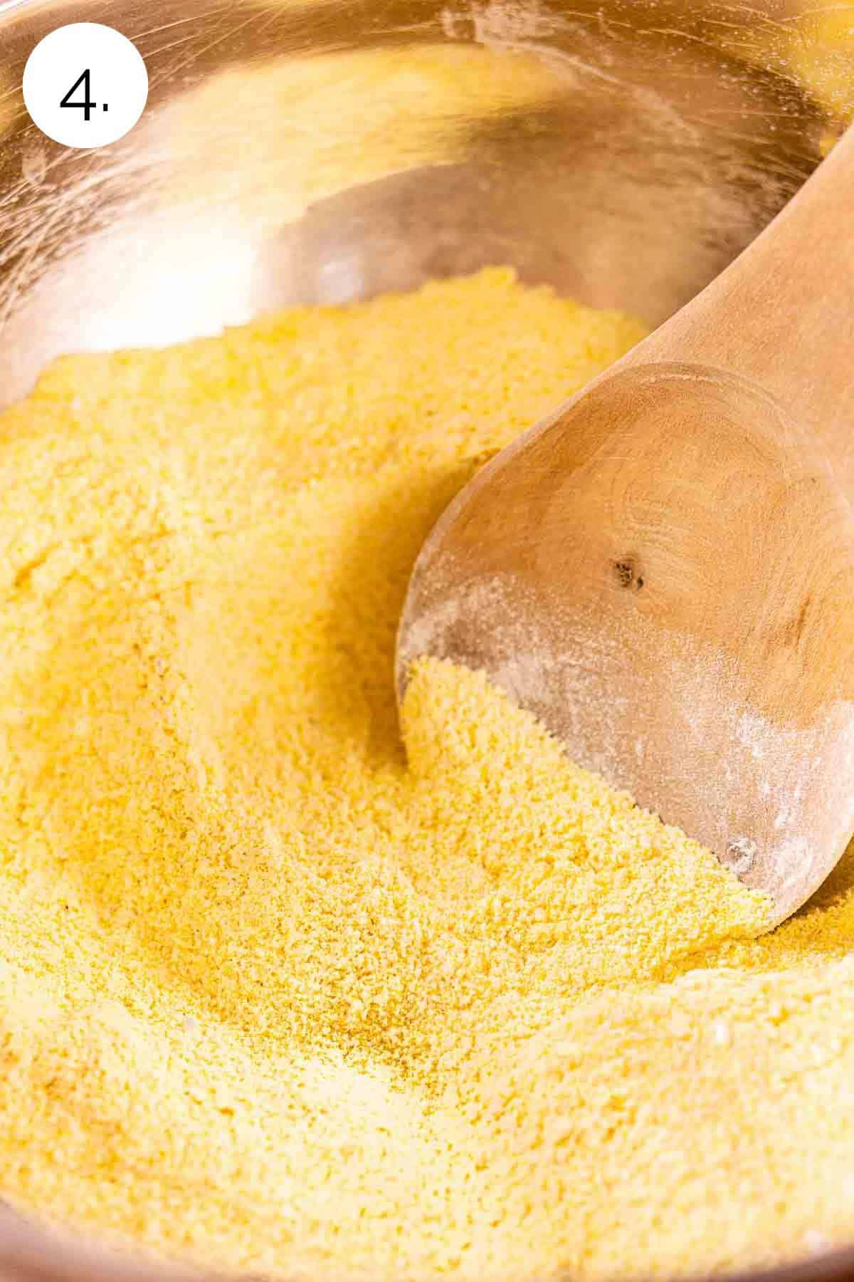 A wooden spoon stirring the dry ingredients in a large stainless mixing bowl.