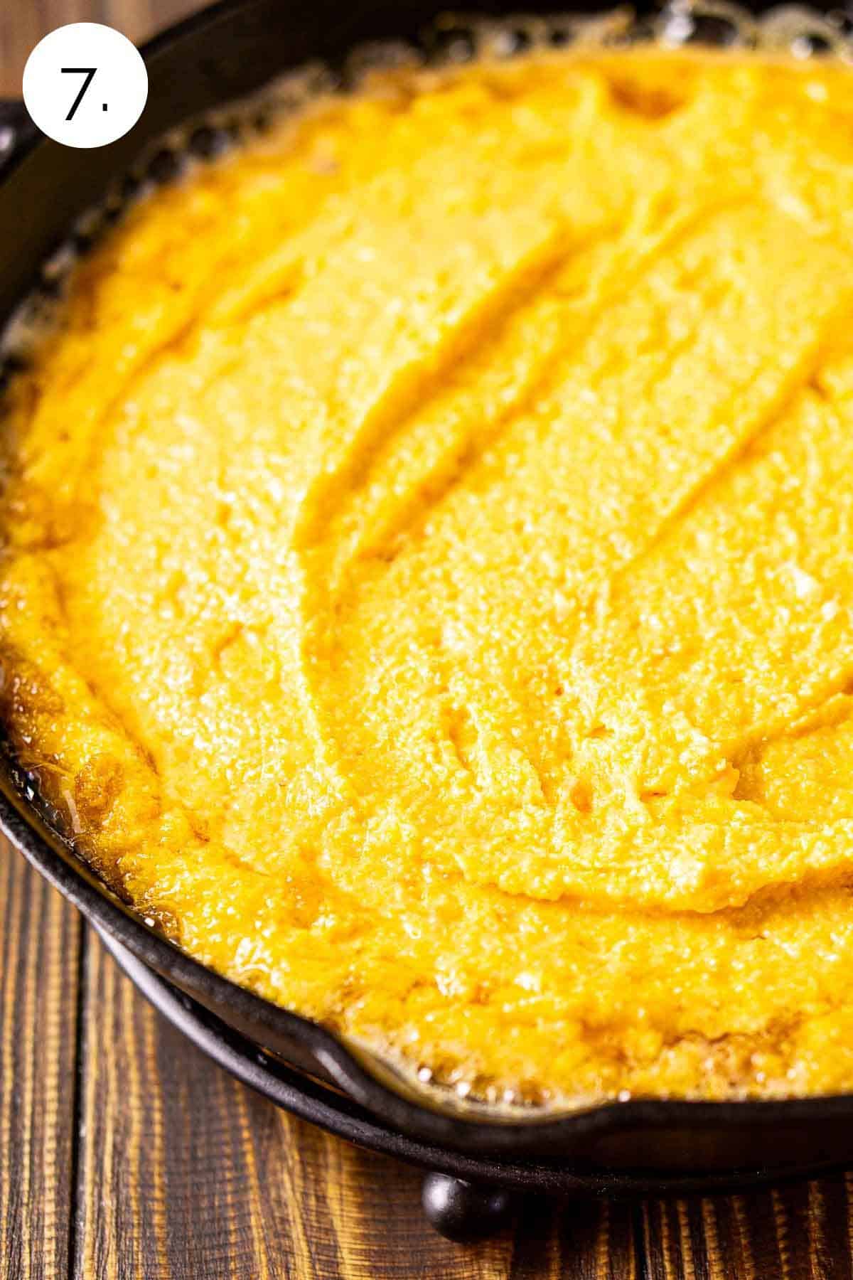 The cornbread batter and melted butter in a black cast-iron skillet on a trivet before it goes in the oven.