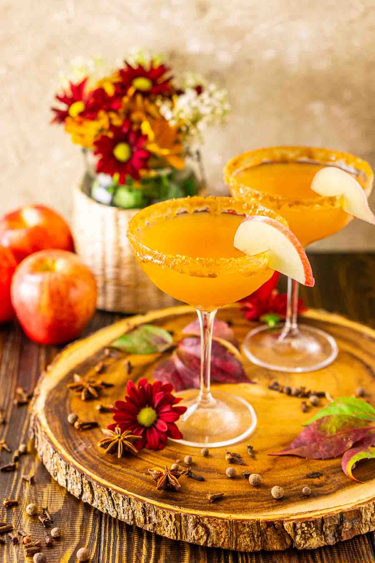 An apple cider martini on a wooden serving tray with fall flower and whole apples in the background.