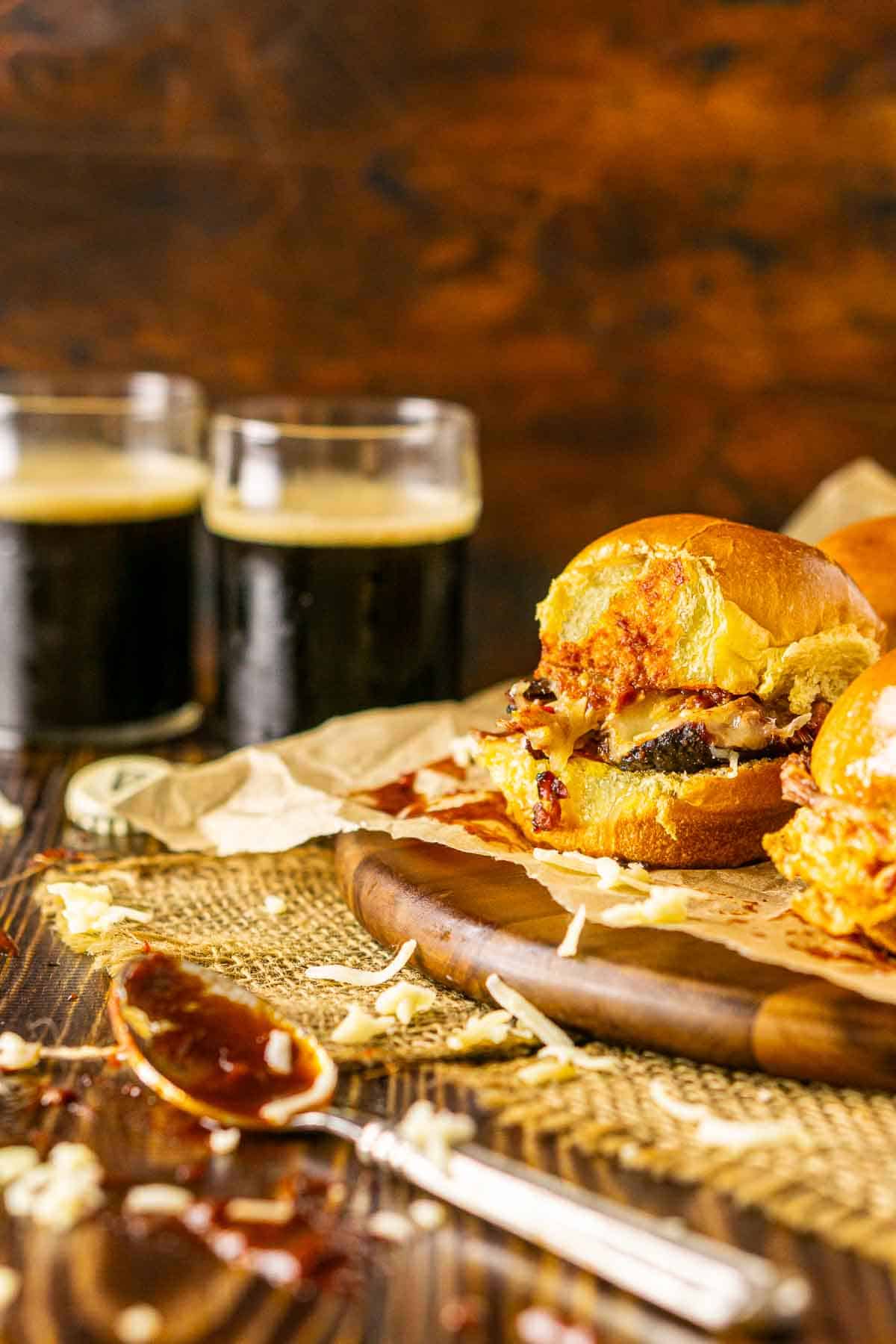 A close-up of the brisket sliders against a wooden background with two beers to the left and smears of BBQ sauce in front.