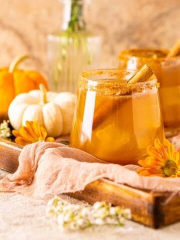 A pumpkin spice margarita with a cinnamon stick garnish on a wooden tray with miniature pumpkins in the background.