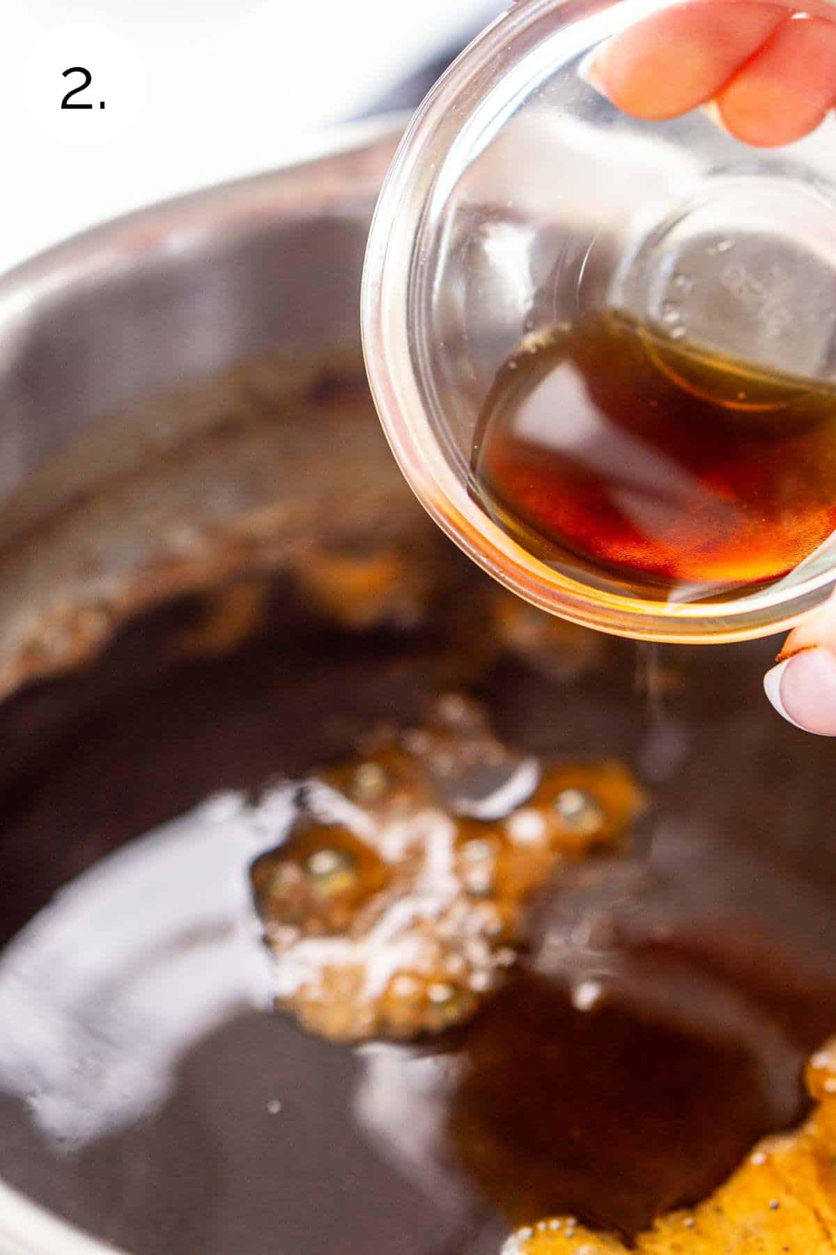 A hand pouring a small bowl of vanilla extract into the saucepan after boiling the mixture.