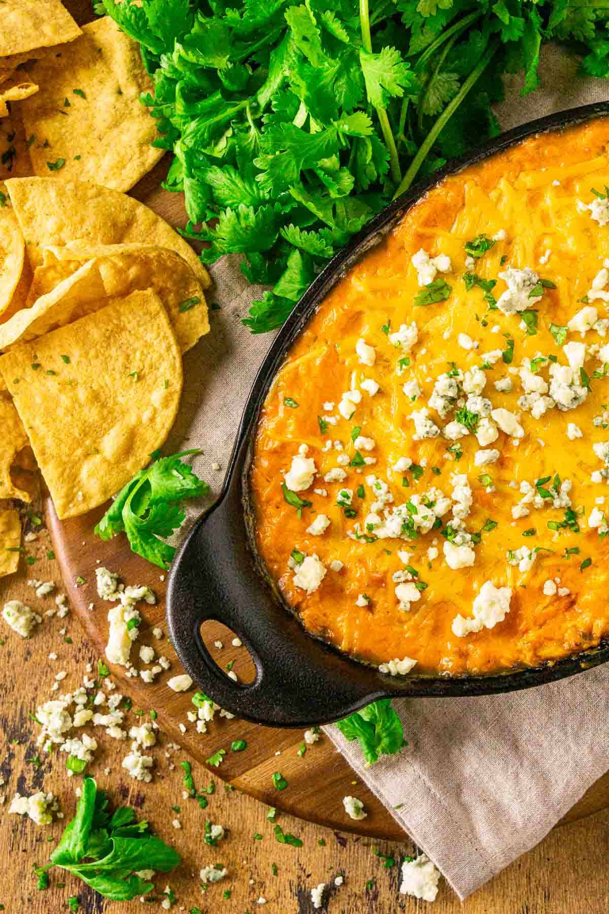 An aerial view of the smoked Buffalo chicken dip on a wooden plate with cilantro and blue cheese scattered around it.