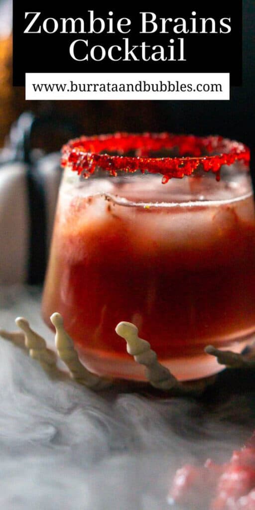 A zombie brains cocktail in a fake skeleton hand with muddled raspberries to the left surrounded by a mist and text overlay on top of the image.
