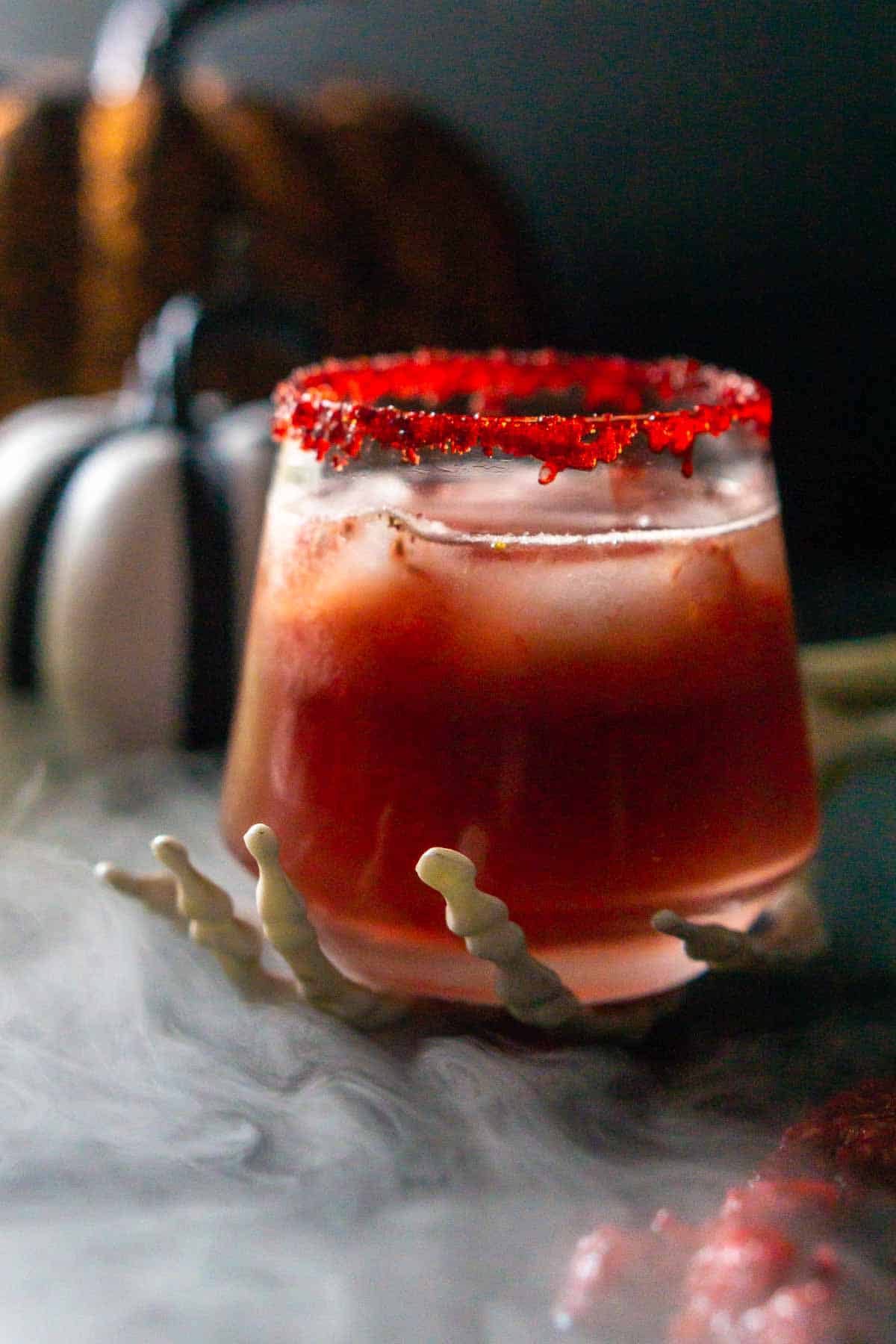 A close-up of a Zombie Brains Halloween cocktail on a skeleton hand with a cloud of mist circling it from the left.