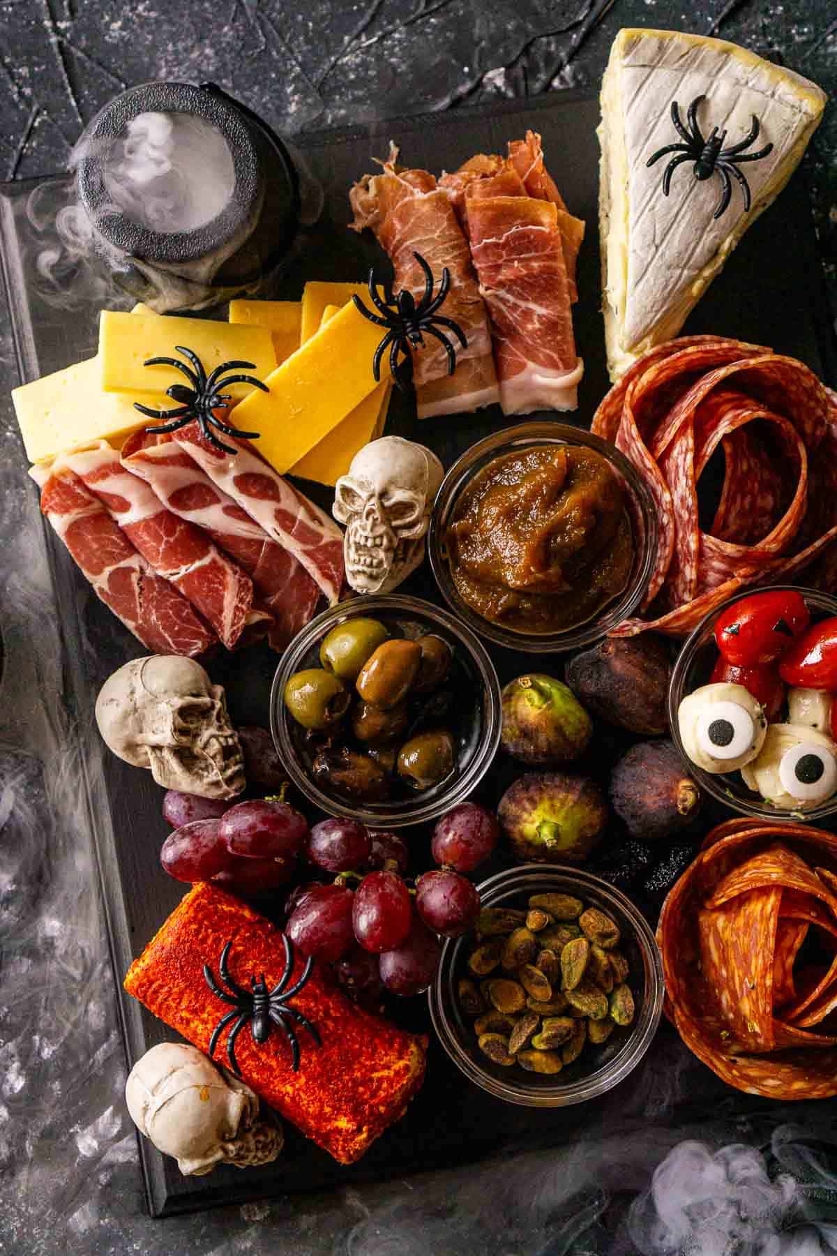 The Halloween charcuterie board on a black and white textured surface with a spooky mist coming in on the sides from dry ice.