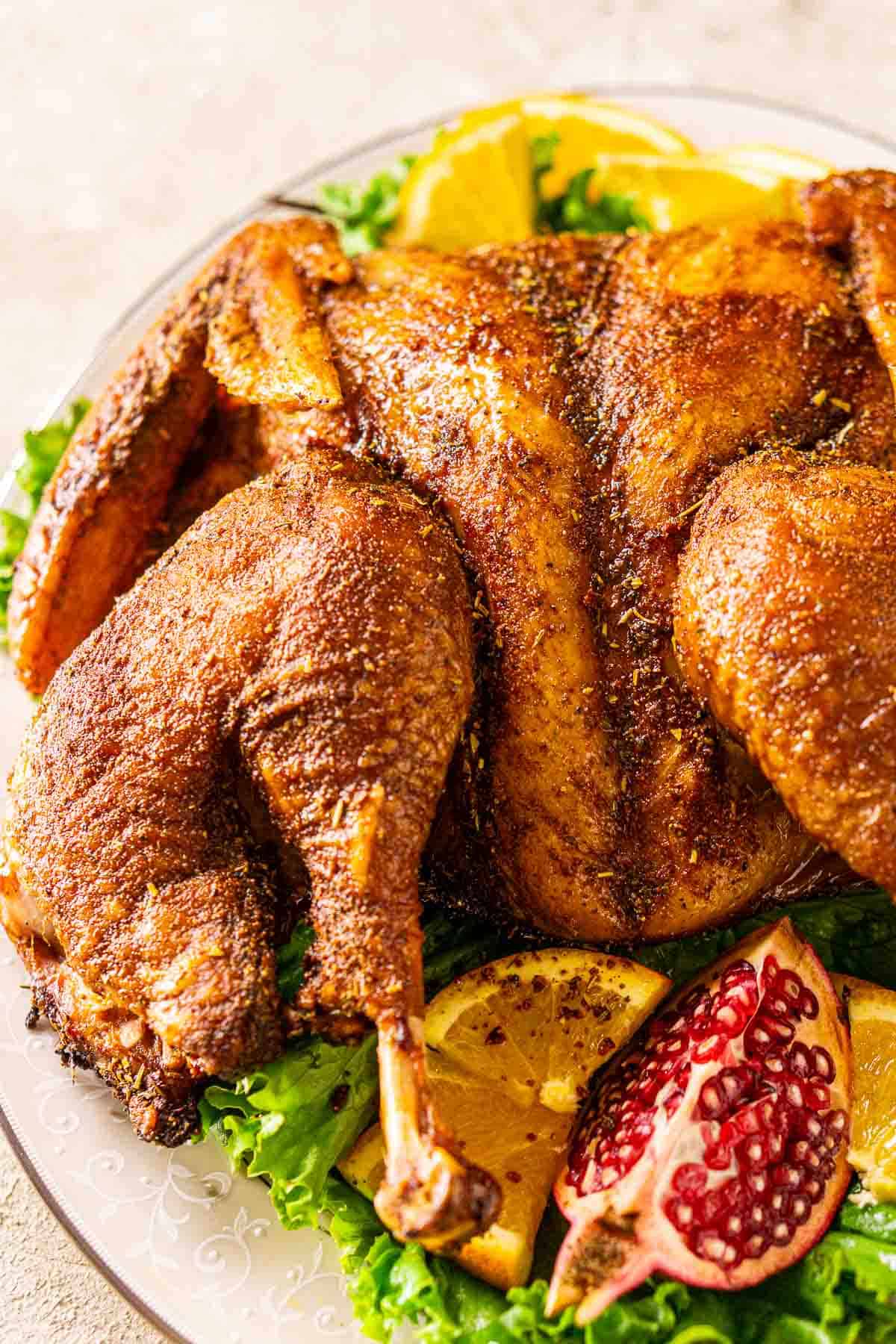 Looking down on the smoked spatchcock turkey on a white platter with green leaf lettuce set on a cream-colored surface.