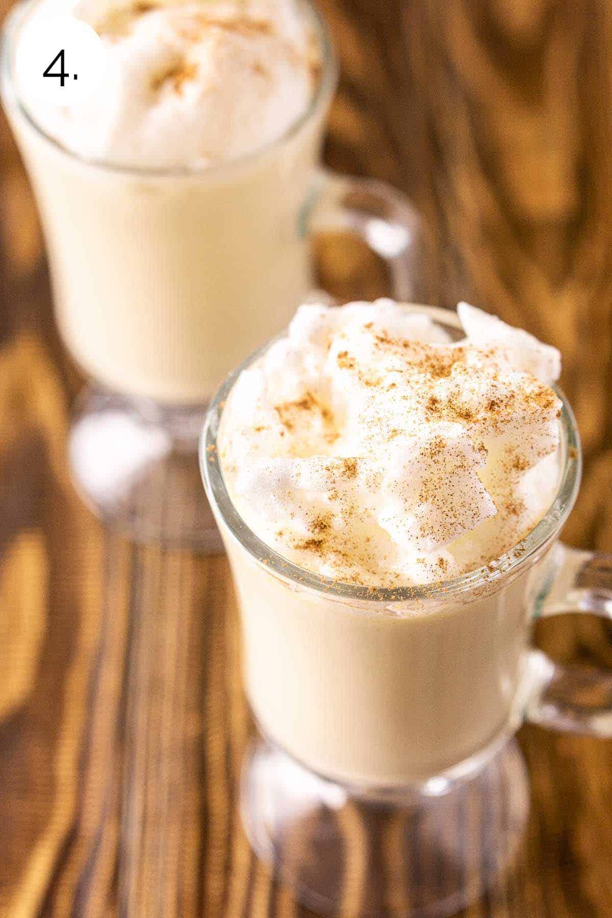 Two glasses of the bourbon eggnog with an egg white topping covered in a dusting of ground cinnamon and nutmeg.