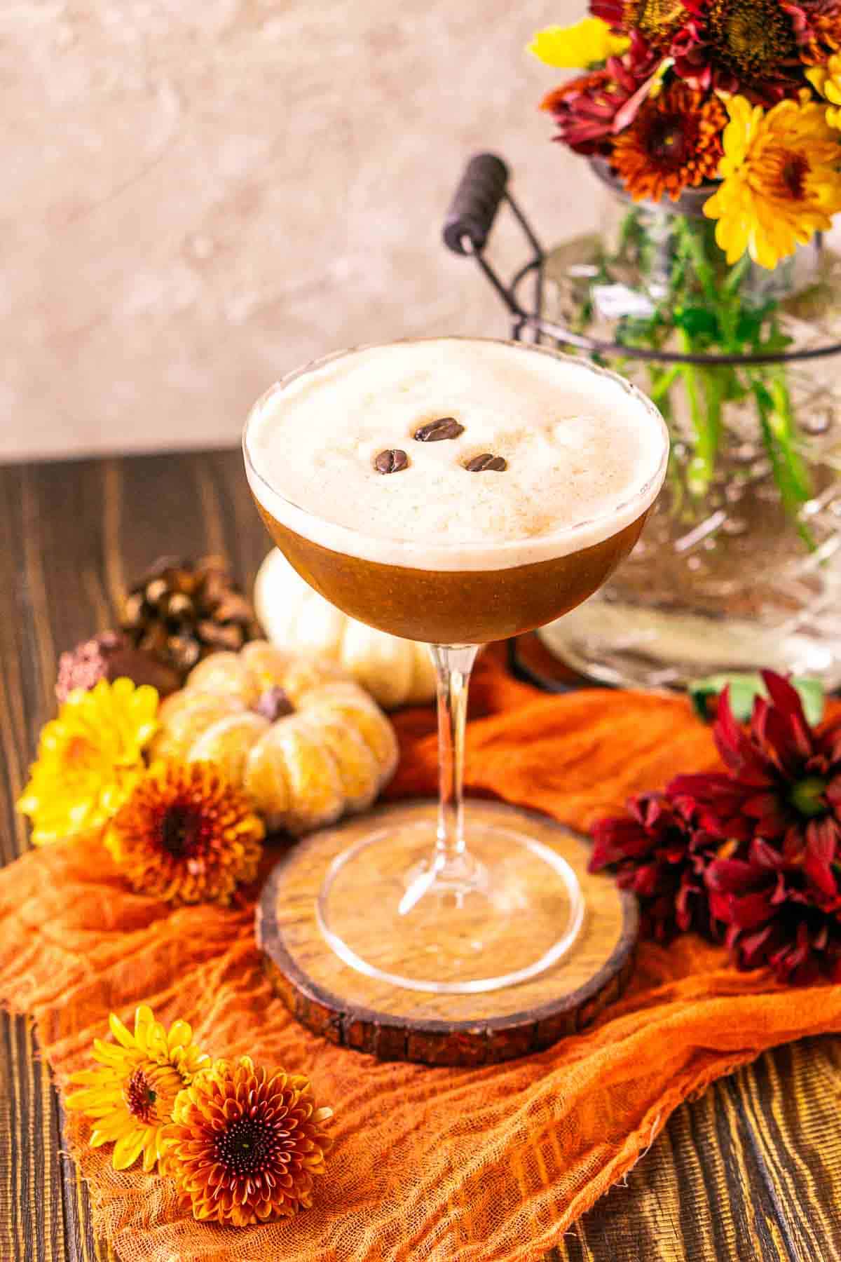 Looking down on a pumpkin spice espresso martini with fall flowers placed around it on orange cloth.