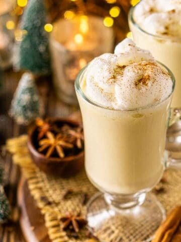 Looking down on a glass of bourbon eggnog with twinkling lights in the background and spices and Christmas decor around the drink.