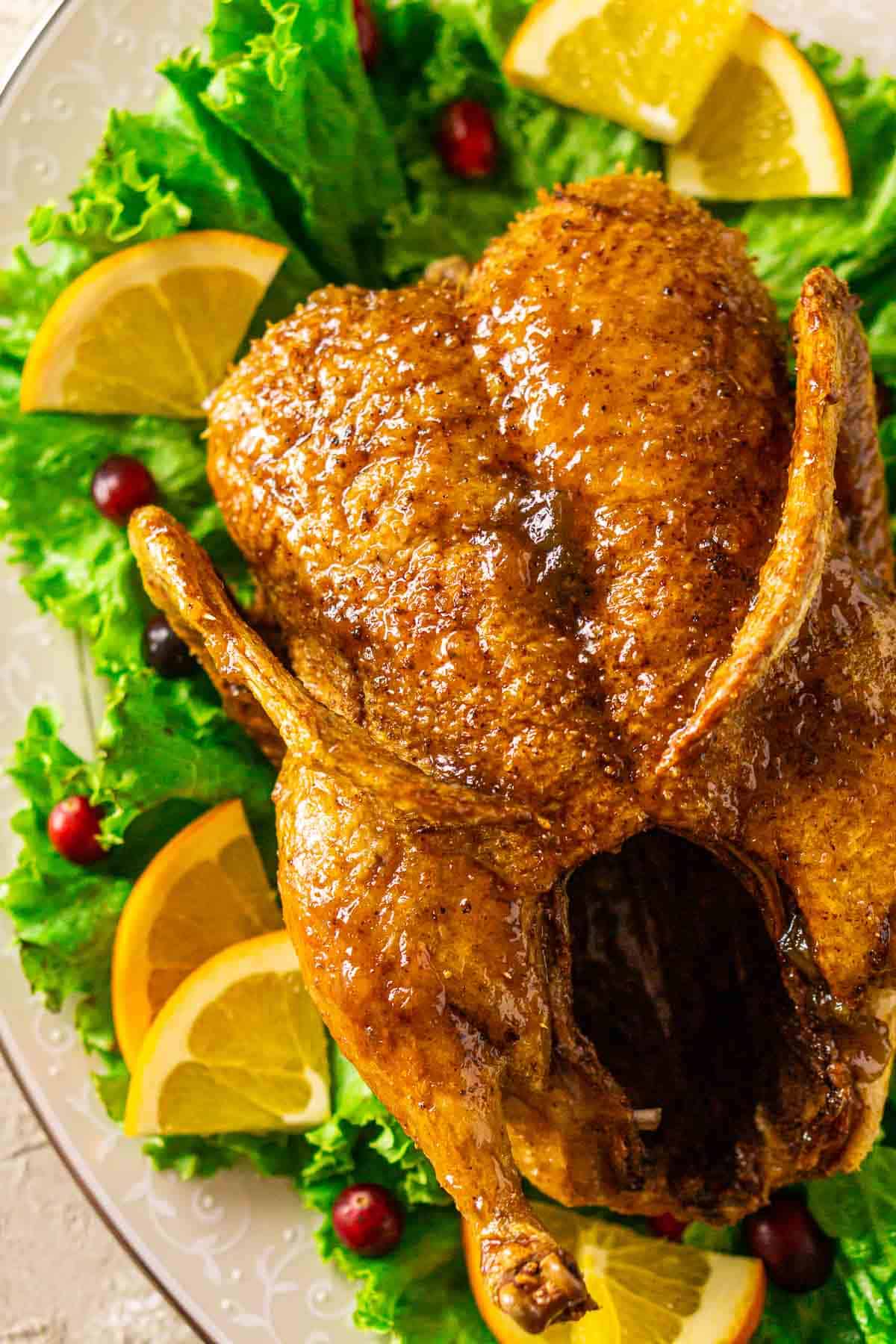 An aerial shot of the deep-fried duck on a white serving platter with green leaf lettuce, orange slices and fresh cranberries.