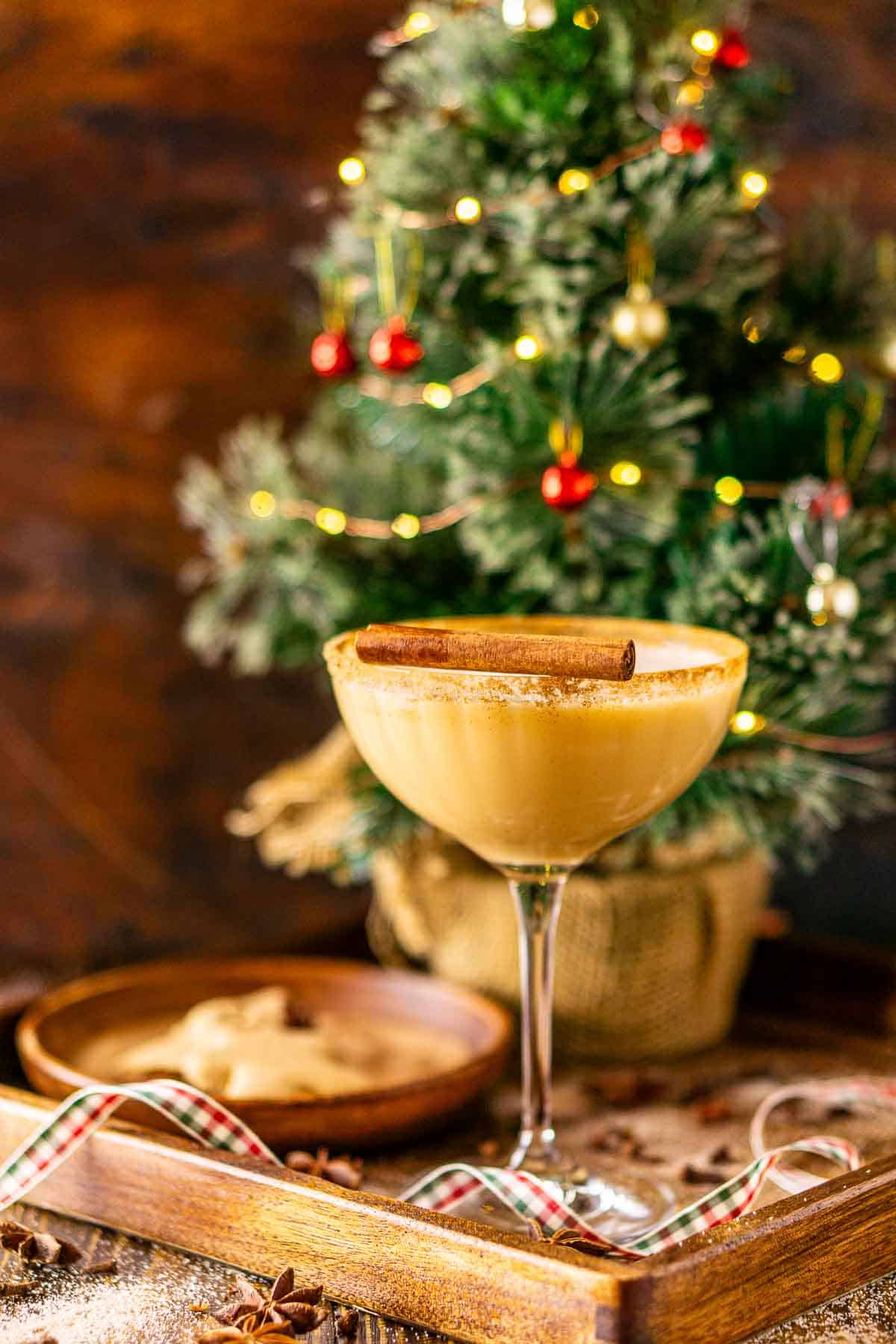 Looking straight on to a gingerbread martini on a wooden tray with a Christmas ribbon in front and spices scattered around it.