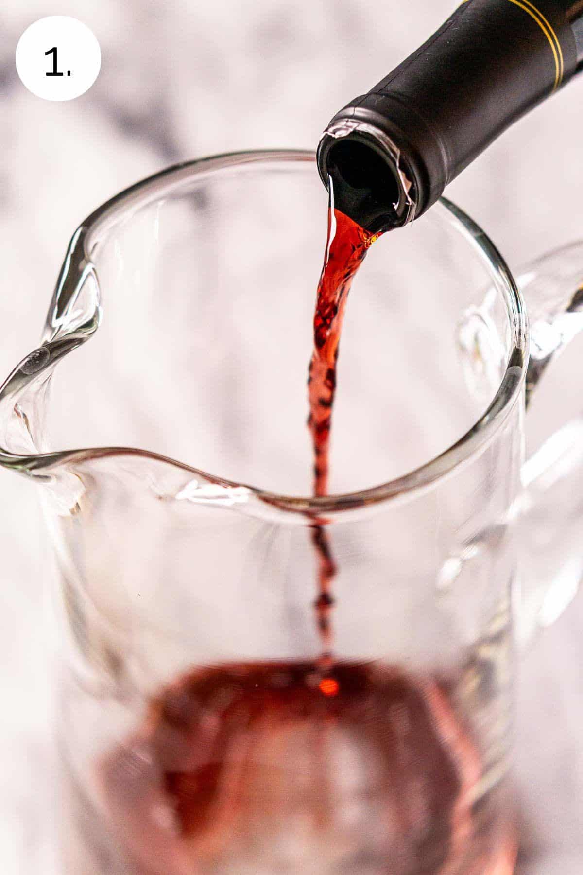 Pouring a bottle of pinot noir into a large glass pitcher on a white marble surface.