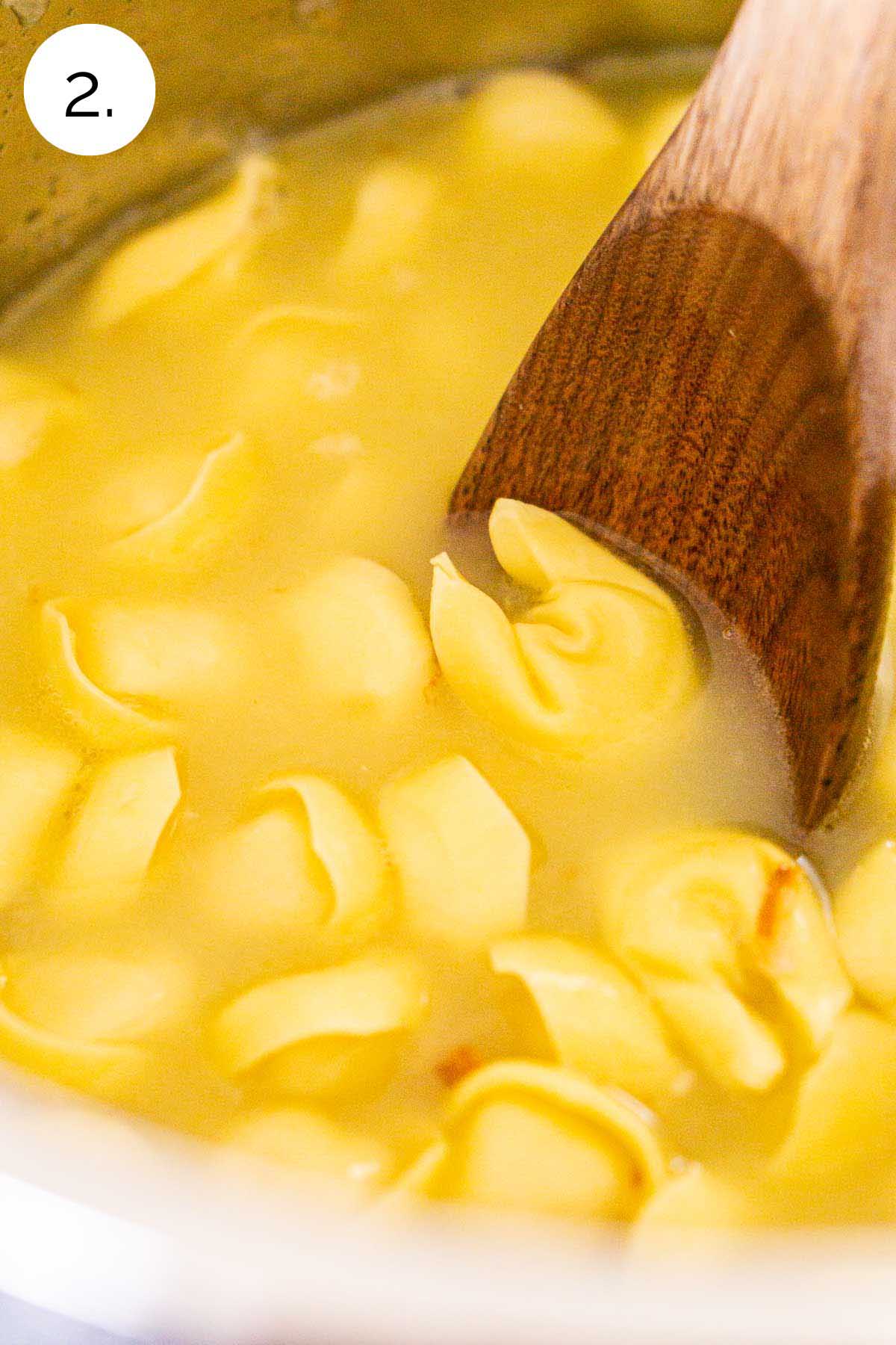 A brown wooden spoon stirring the fresh cheese tortellini in chicken stock before cooking at high pressure.
