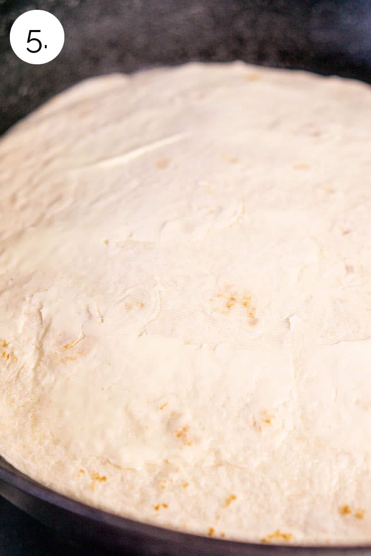 The top of the tortilla in a black cast-iron skillet as it cooks on the first side on the stove-top.