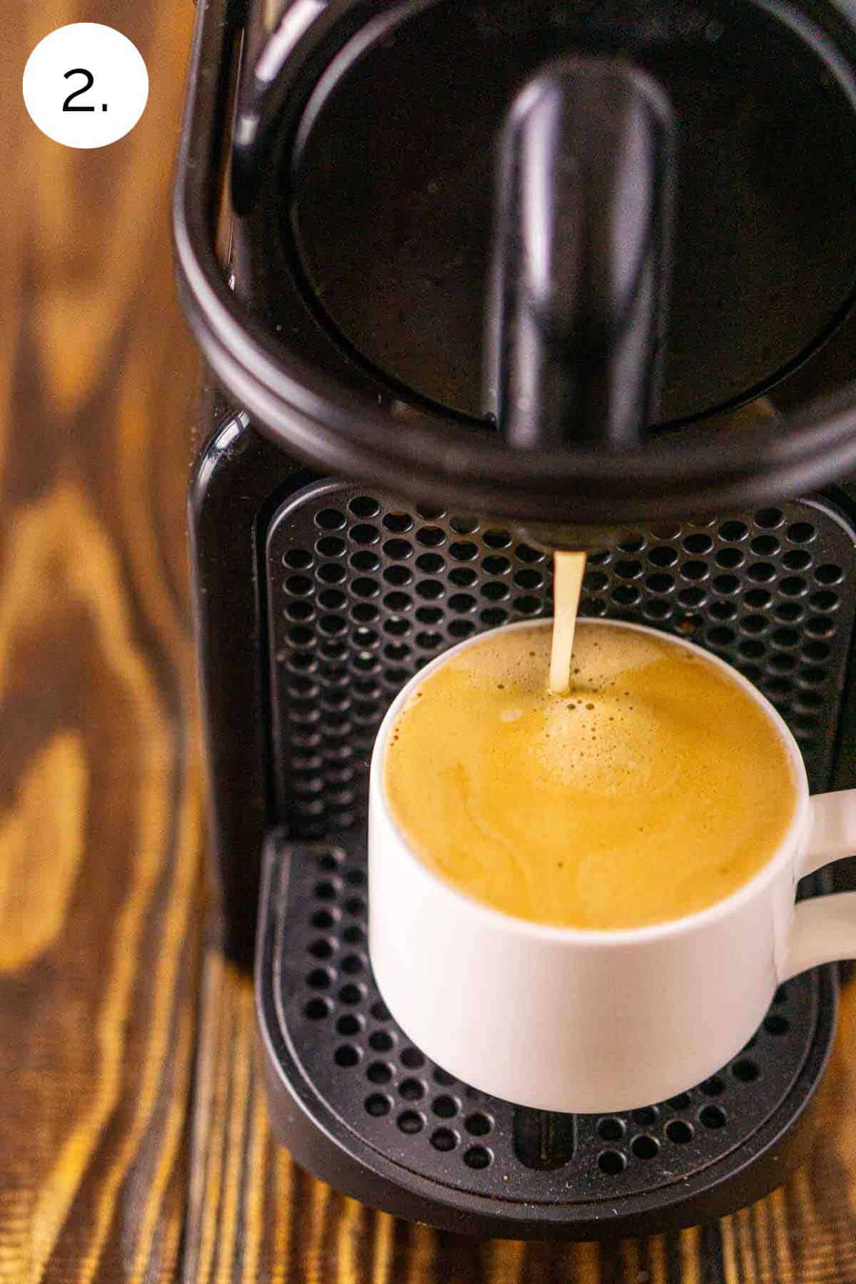 A Nespresso machine making a fresh cup of espresso on a brown wooden surface.