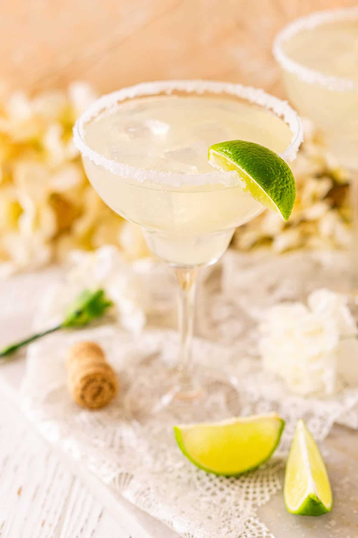 A close-up view of a prosecco margarita on a piece of white lace with lime slices in front to the right.