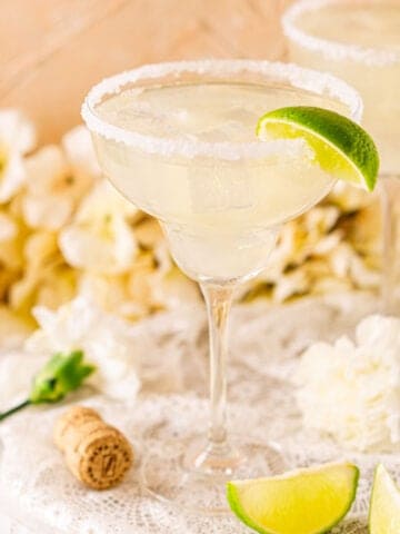 A prosecco margarita on a white marble board with a cork to the left and lime slices on the right.