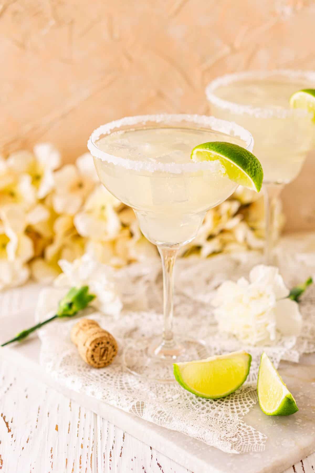A prosecco margarita on a white marble board with a cork to the left and lime slices on the right.