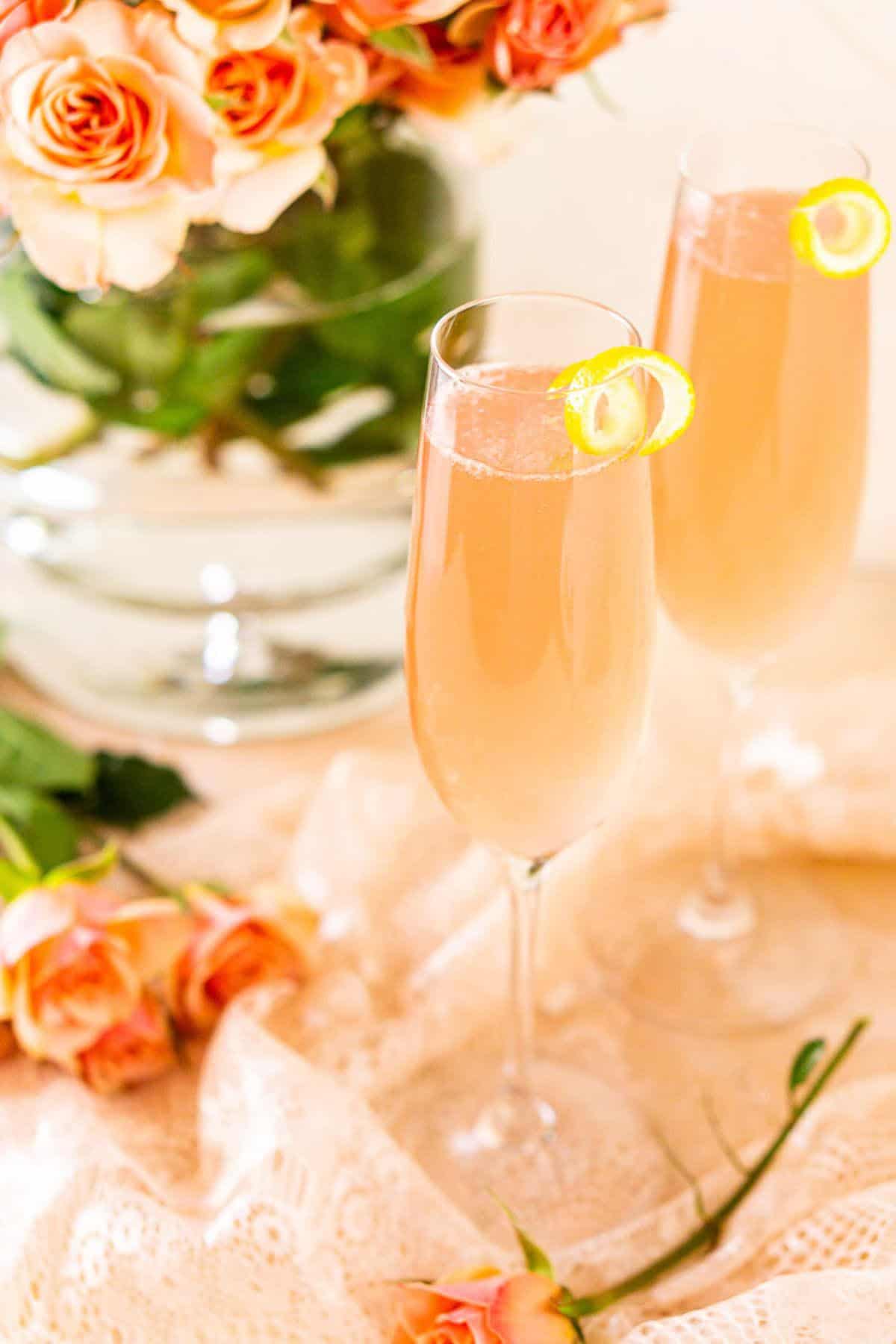Looking down on a sparkling rosé French 75 with a bundle of pink roses sitting on a bundle of pink lace.