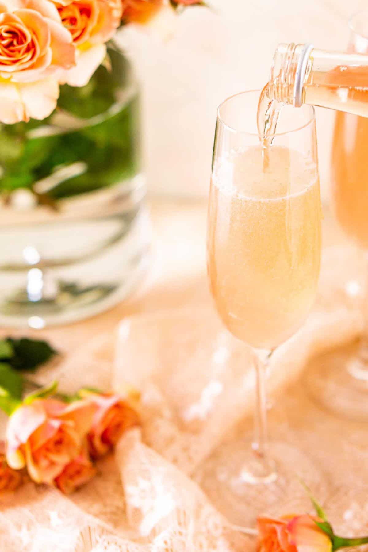 Pouring the sparkling rosé into the cocktail mixture in a Champagne flute on top of a bed of pink lace.