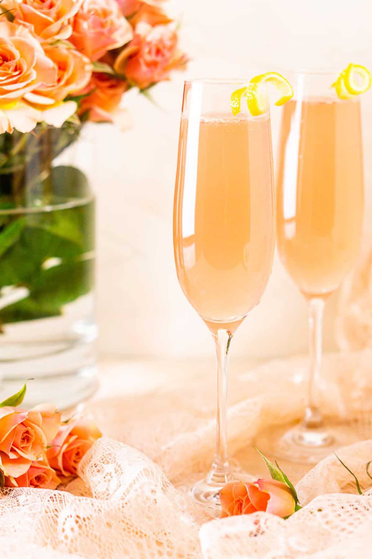 A close-up shot of a sparkling rosé French 75 with a vase of pink roses in the background.