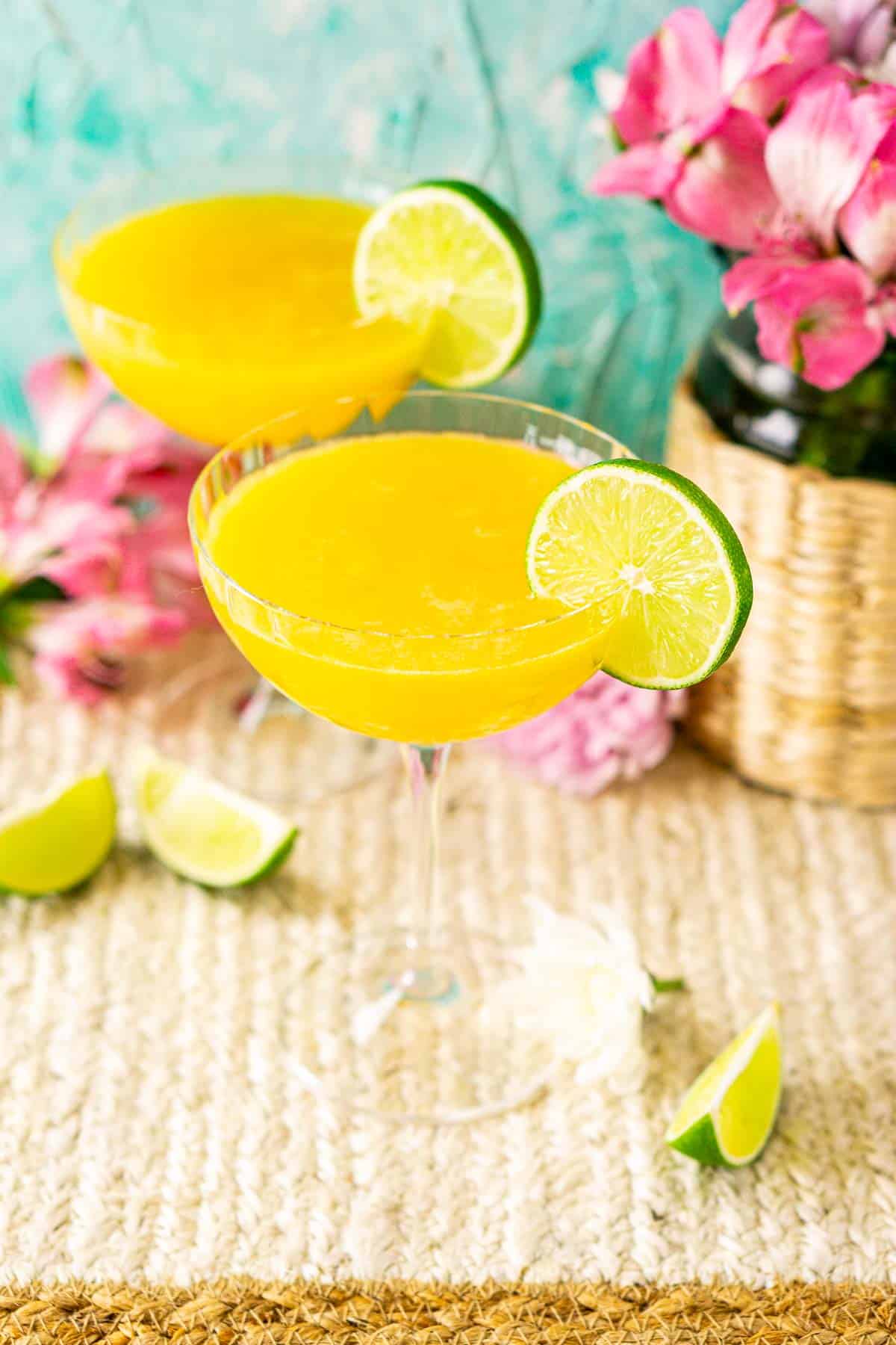 Looking down on two passion fruit daiquiris with a white flower to the side and several lime slices scattered around them.