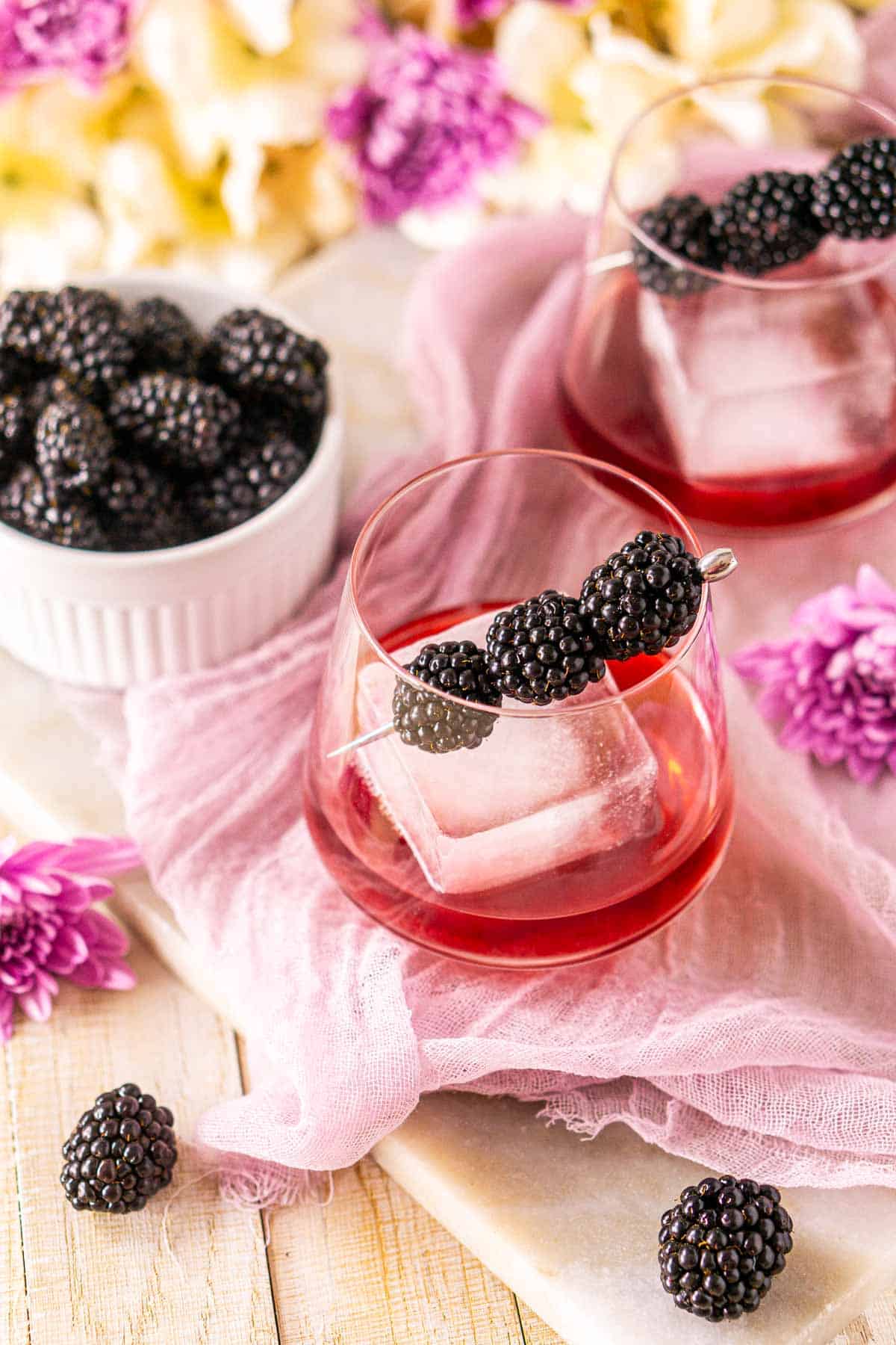 Looking down on a blackberry old fashioned on a white marble board with fresh berries scattered around it.