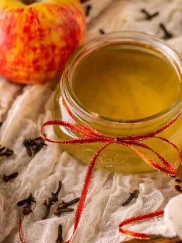 A glass mason jar filled with the spiced apple simple syrup on a wooden serving tray with fall spices surrounding it.