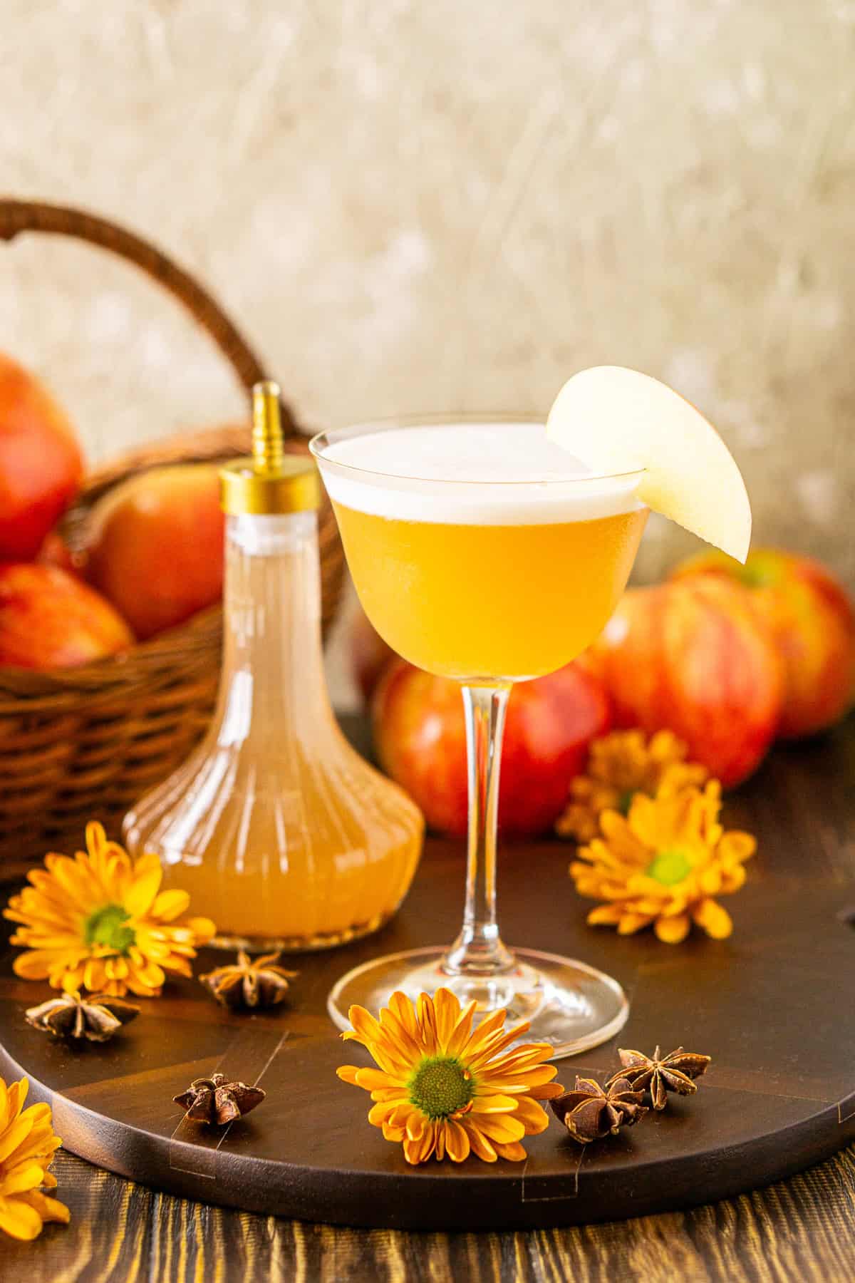 A straight-on view of the apple cider whiskey sour with a basket of apples behind it and fall flowers around it.