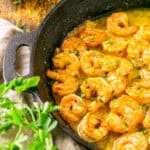 The smoked shrimp in a garlic butter sauce in a black cast-iron skillet with parsley and a bowl of Cajun seasoning on the side.