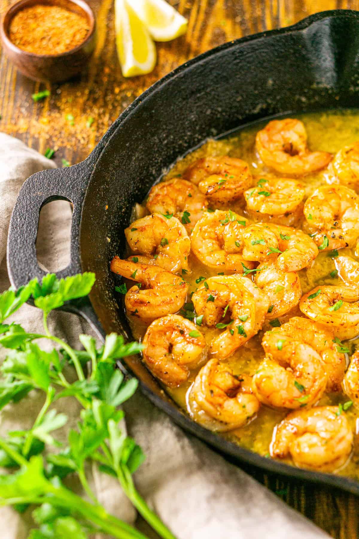 The smoked shrimp after cooking in a black cast-iron skillet with parsley sprinkled on top of a bowl of Cajun seasoning in the background.