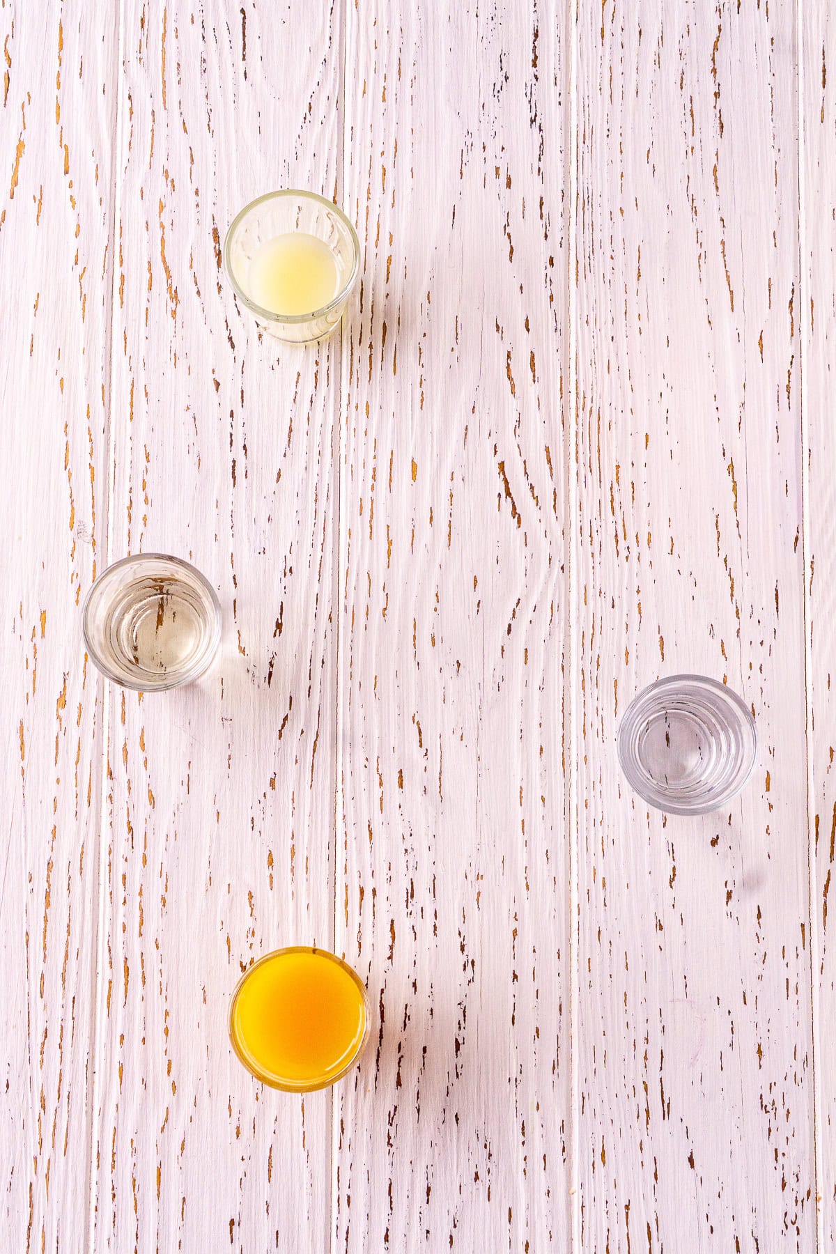 The ingredients for the passion fruit daiquiri in clear shot glasses on a white wooden board.