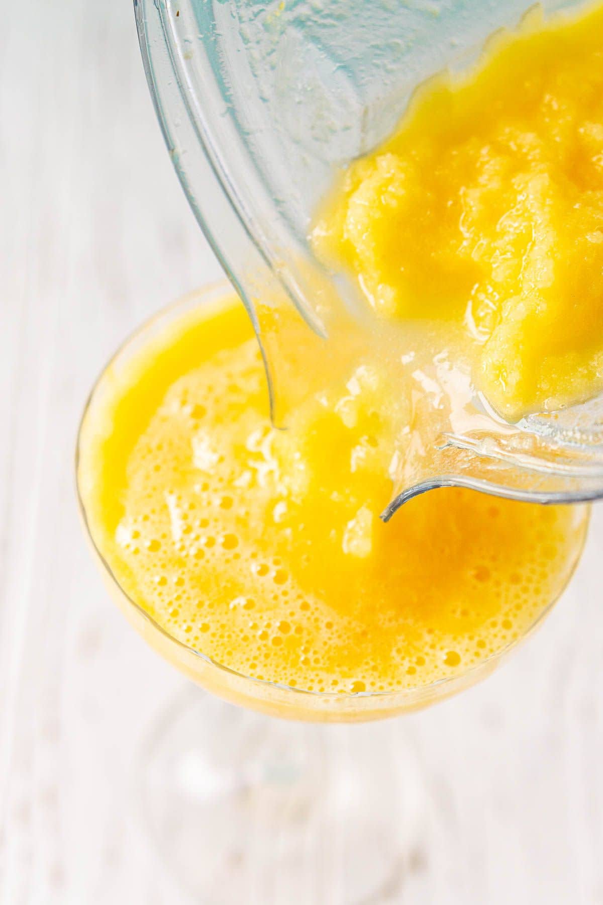 Pouring the frozen passion fruit daiquiri from the blender into the cocktail glass to serve.