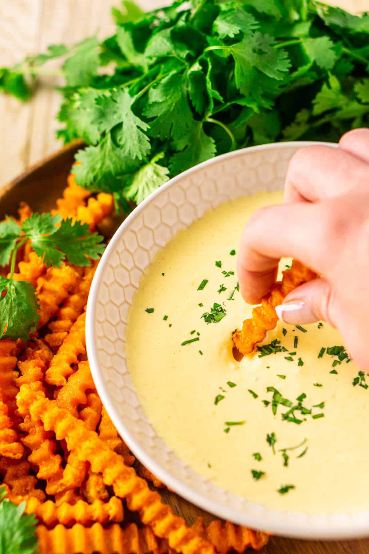 A hand dipping a sweet potato fry into a bowl of mango-habanero aioli.