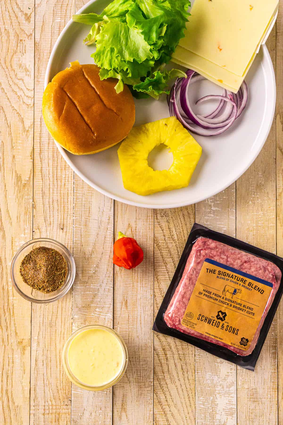 The ingredients to make jerk burgers set out on a cream-colored wooden surface.