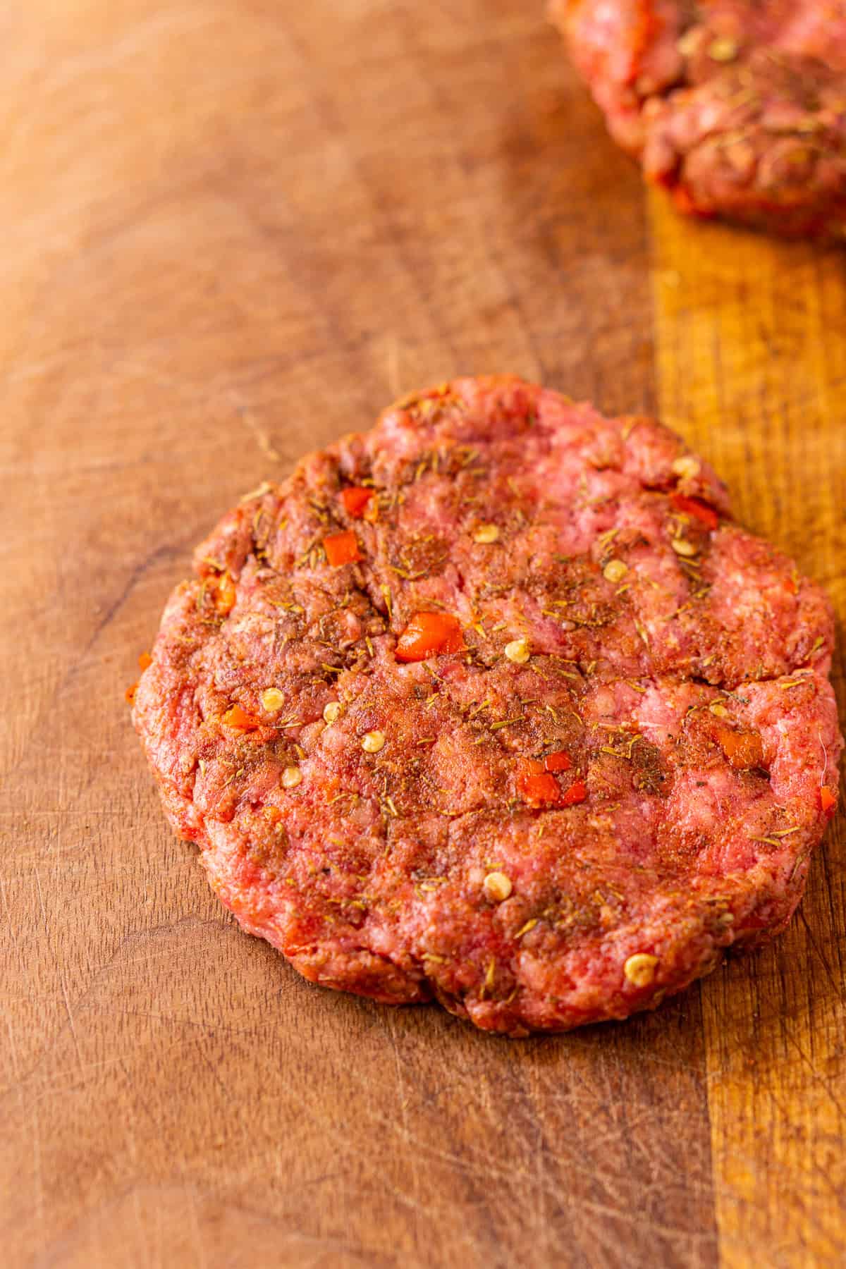 A jerk burger patty after it's been shaped on a brown wooden cutting board before it goes on the grill.