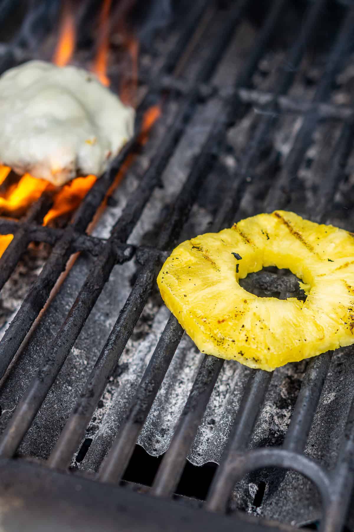 A pineapple ring and burger covered in cheese on a black grill as they cook.