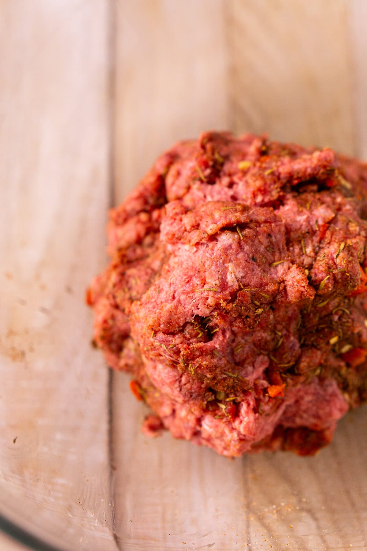 The ground beef in a glass mixing bowl after it's been combined with the dry jerk seasoning.