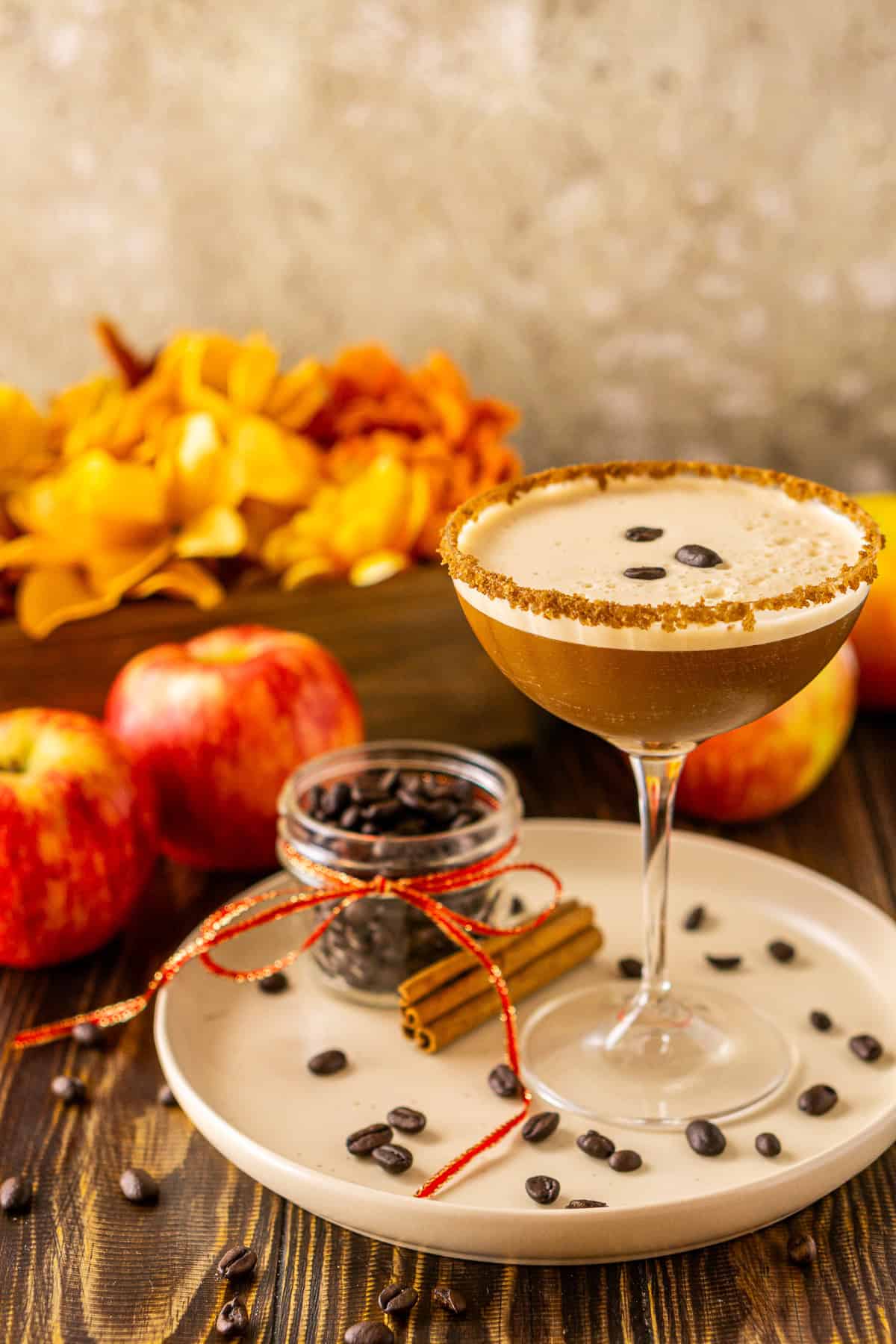 A spiced apple espresso martini on a cream-colored plate with apple and fall flowers in the background.